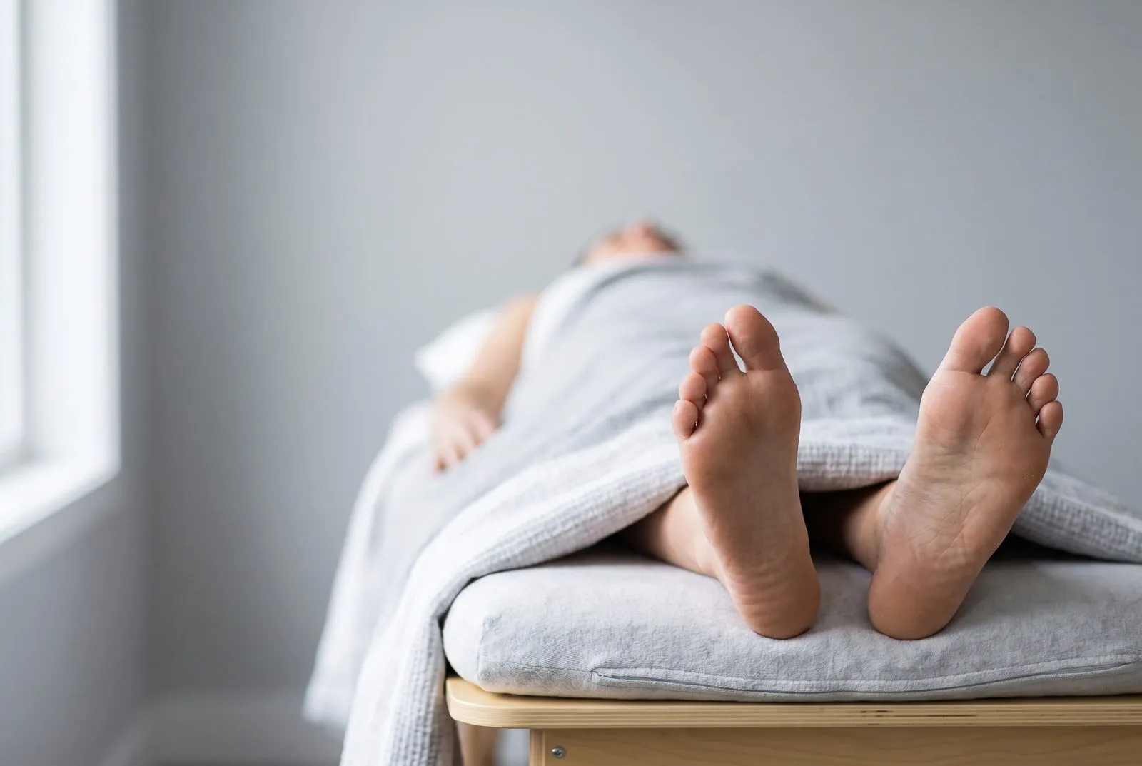 En person vilar på en behandlingsbänk under en filt, med bara fötter i förgrunden